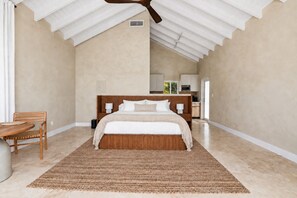 Un dormitorio con una cama grande, un cabecero de madera, una mesita de noche, una silla y un ventilador de techo.