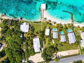 An aerial view of a resort with multiple buildings, a beach, and clear turquoise waters. - Beachfront Bungalow with Pool for Couples (George Town)
