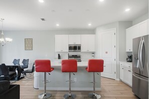 A modern kitchen with white cabinets, a stainless steel refrigerator, and a bar area with red chairs. - Perfect 6-bedroom house with games in welcoming Davenport (Davenport)