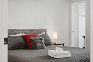 A neatly made bed with a grey headboard, a red pillow, and a grey throw pillow. There is a small bedside table with a lamp and a folded white towel on the bed. - Perfect 6-bedroom house with games in welcoming Davenport (Davenport)