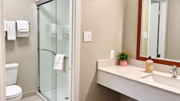 A bathroom with a glass-enclosed shower, a white toilet, a sink with a mirror, and a small potted plant.