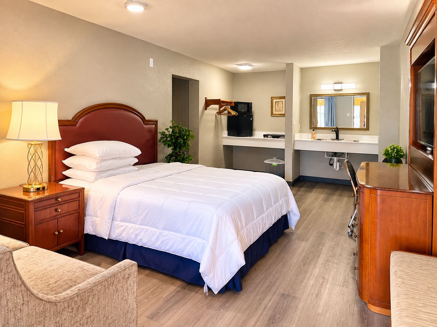 A hotel room with a bed, bedside table, lamp, chair, desk, and a mirror.