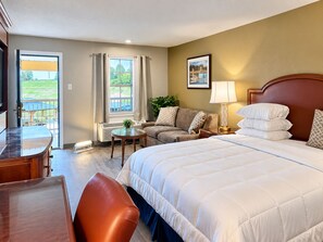 A hotel room with a bed, a desk, a chair, a sofa, a lamp, and a window with curtains. - Remington Inn and Extended Stay (Little Rock)
