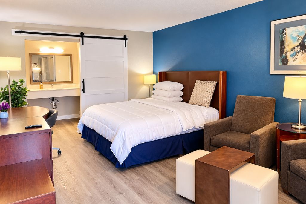 Ein Hotelzimmer mit Bett, Schreibtisch, Stuhl, kleinem Tisch und einem an der Wand befestigten Fernseher.