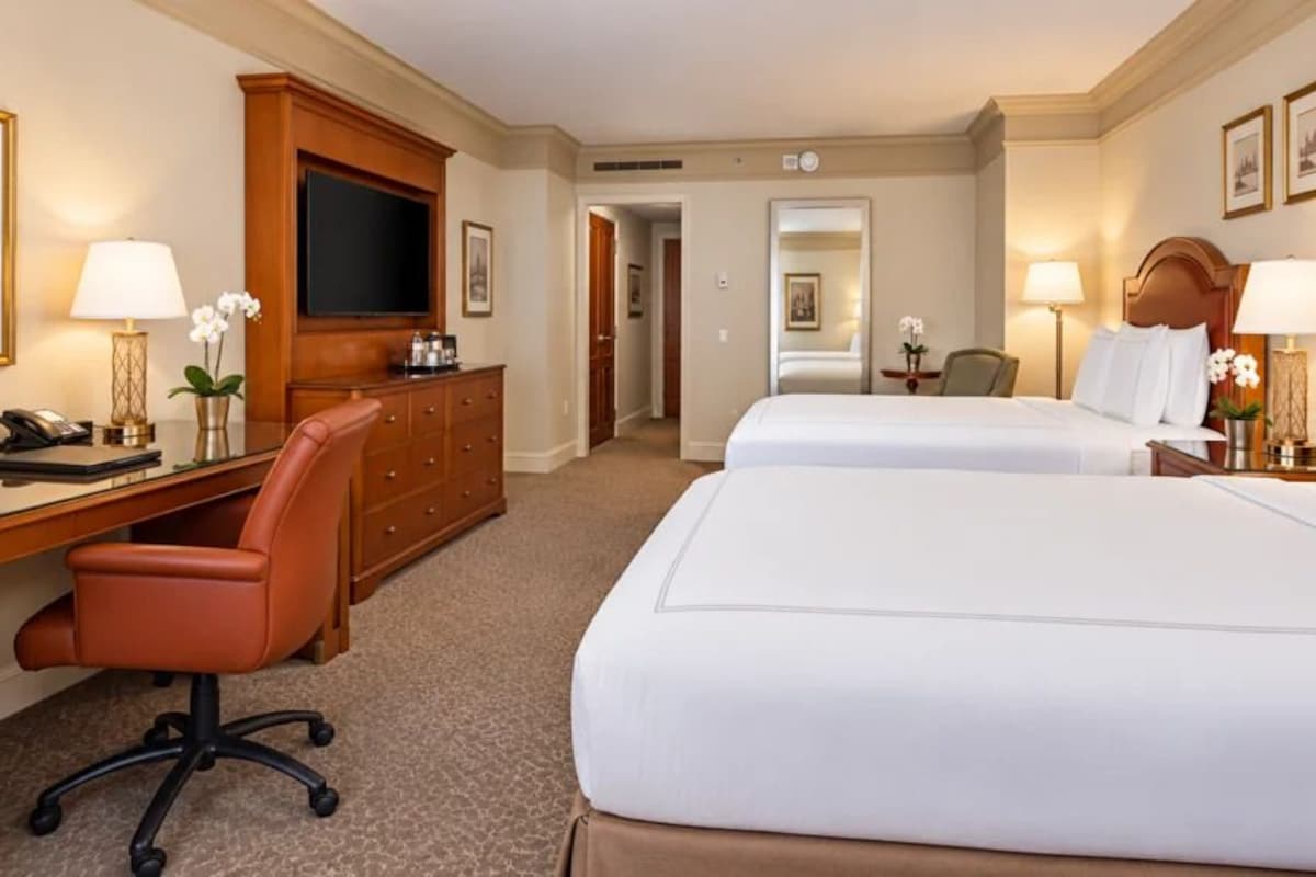 A hotel room with two beds, a desk with a chair, a television, and a desk lamp.