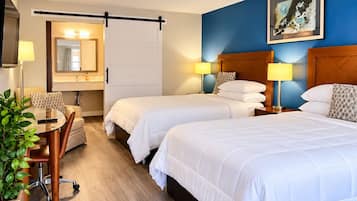 A hotel room with two beds, a desk with a chair, a mirror, and a painting on the wall.