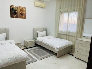 A bedroom with two beds, a bedside table, a dresser, and a window with sheer curtains. - 3-bedroom apartment in soothing Sousse with AC for relaxing stays (Susah)