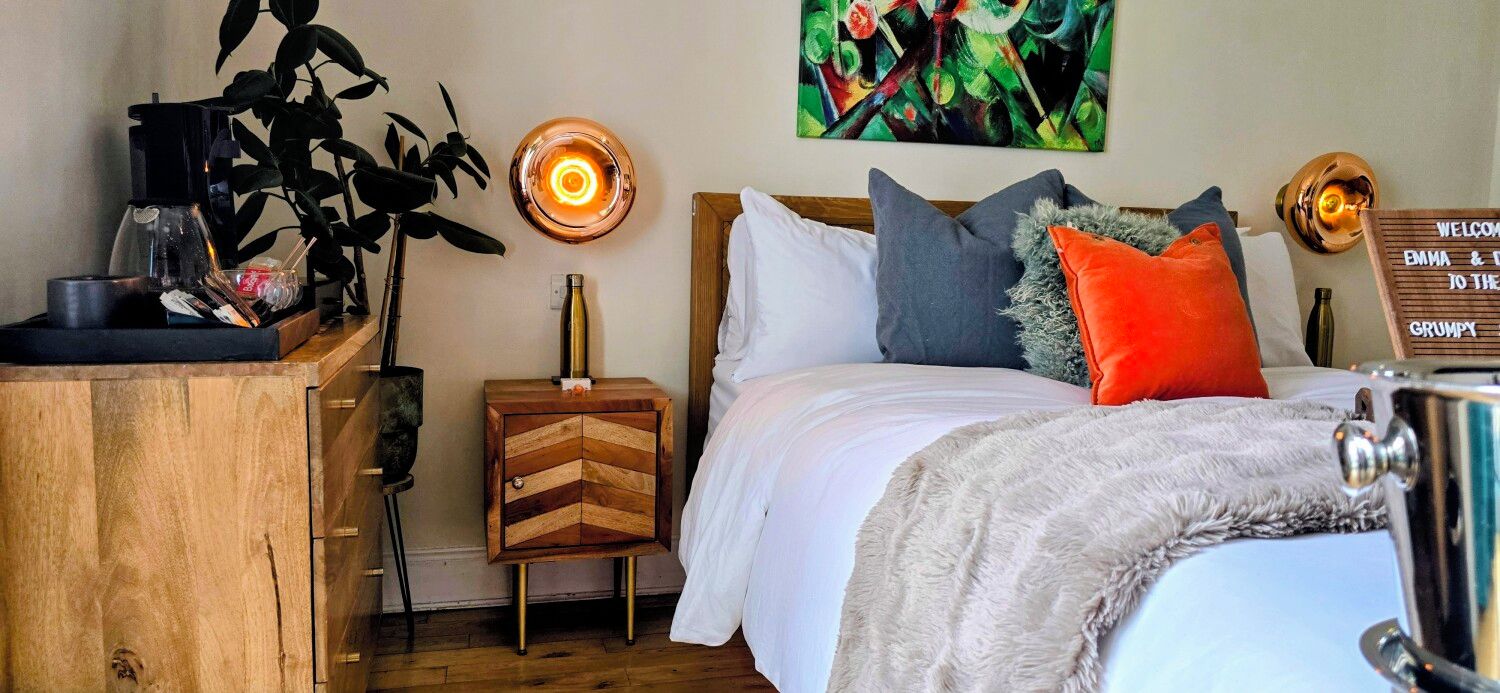 A bedroom with a bed, bedside table, lamp, and a wall-mounted sign.