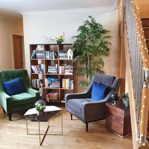 Una sala de estar con dos sillones, una estantería, una planta en maceta y una escalera decorada con luces.