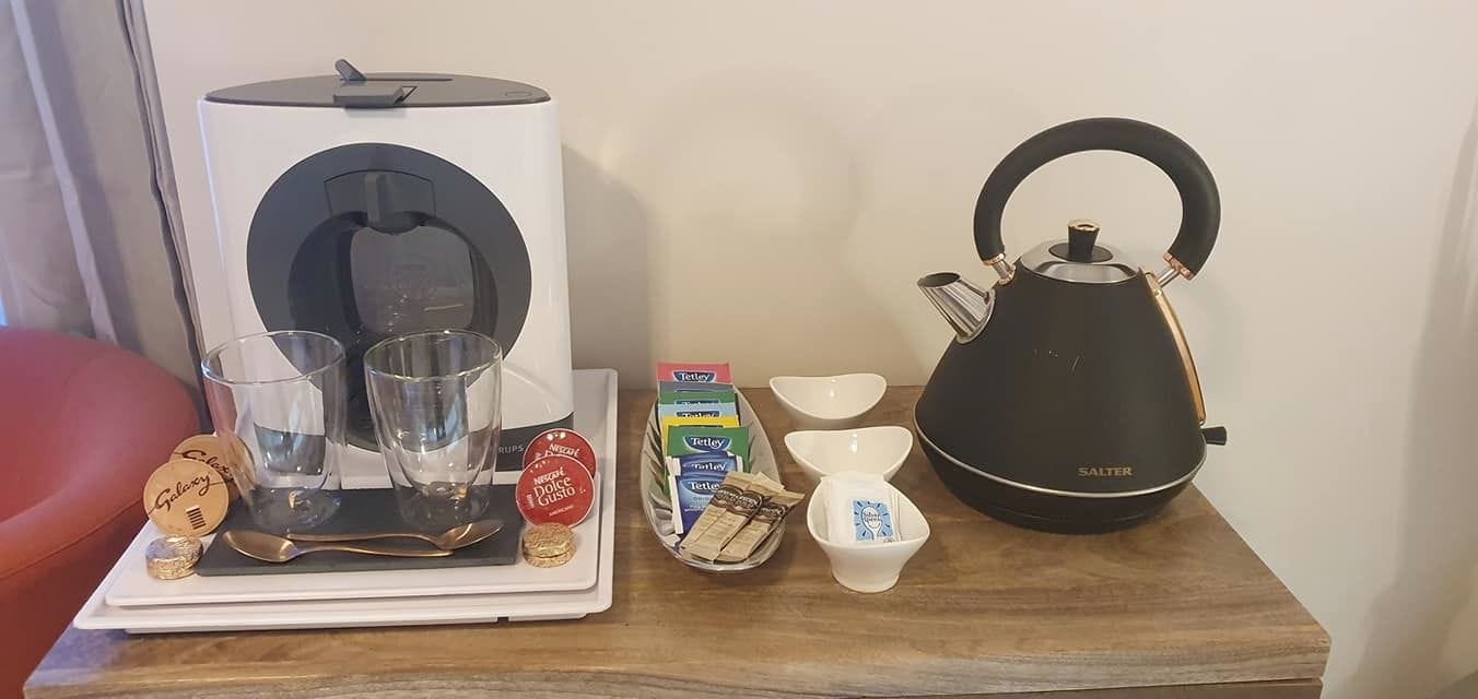 A tray with a coffee maker, glasses, a teapot, and some food items on a wooden table.