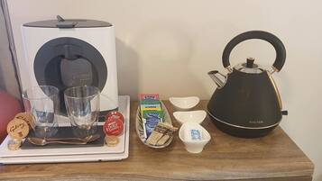 A tray with a coffee maker, glasses, a teapot, and some food items on a wooden table.