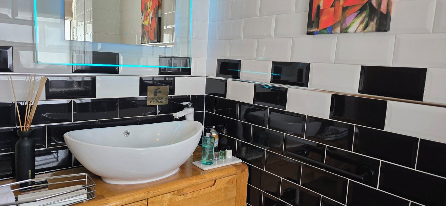 Uma casa de banho moderna com uma grande lavatório em forma de taça branca, azulejos preto e branco, um espelho com moldura azul e uma pequena placa de aviso.
