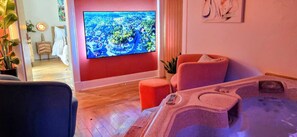 A room with a large flat-screen TV, a massage chair, and a small table with a remote control.