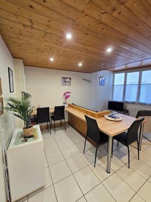 A dining area with a wooden table, black chairs, a small potted plant, and a counter with a television. - A cozy little nest in Mont-Dore (Mont-Dore)