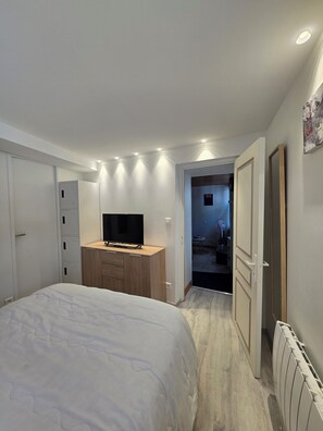 A bedroom with a bed, a TV, a wardrobe, and a door leading to another room. - A cozy little nest in Mont-Dore (Mont-Dore)