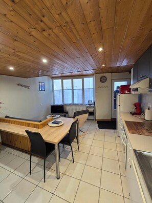 A kitchen with wooden ceiling, a dining area with a wooden table and chairs, and a view through the window. - A cozy little nest in Mont-Dore (Mont-Dore)