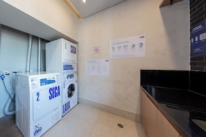 A laundry area with two SECA washing machines, a wall-mounted dryer, and a black countertop. - Spot by Bhomy (São Paulo)