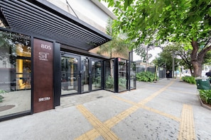 A modern building with a glass entrance, a visible address number, and a clear pathway with tactile paving. - Spot by Bhomy (São Paulo)