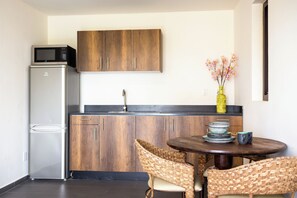 A compact kitchen with a refrigerator, microwave, wooden cabinets, a sink, and a dining area with chairs and a table. - Casa Pasha - Apartment Havana - Jan Thiel (Jan Thiel)