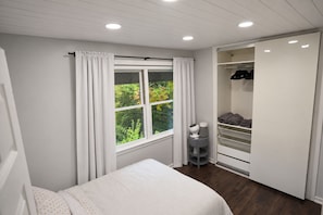A bedroom with a bed, a window with curtains, a closet with shelves, and a bedside table with a lamp. - Charming 3-bedroom house in peaceful Monson (Monson)