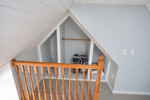 A room with a sloped ceiling, a wooden staircase railing, and a closet with hanging bags. - Charming 3-bedroom house in peaceful Monson (Monson)