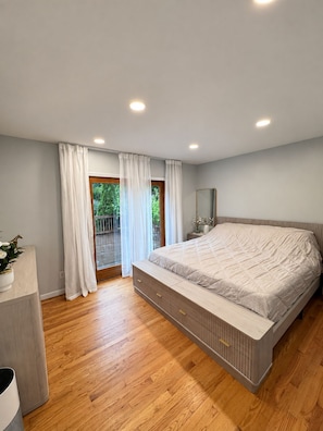 A bedroom with a large bed, wooden flooring, a window with curtains, and a small bedside table. - Charming 3-bedroom house in peaceful Monson (Monson)