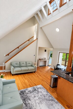 A spacious loft with a high ceiling, a staircase, a living area with a sofa and a coffee table, and a kitchen area with a countertop. - Charming 3-bedroom house in peaceful Monson (Monson)