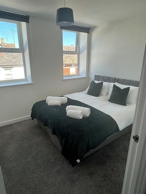 A bedroom with a bed, two windows, a hanging light fixture, and a view of the outside. - 1BR Flat in Andover | Near Local Amenities (Hampshire)