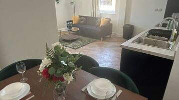 A dining area with a table set for four, a sofa in the background, and a kitchen area with a sink.