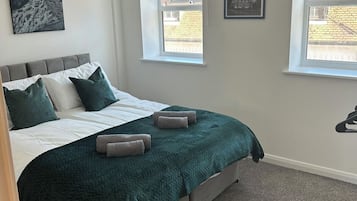 A bedroom with a bed, two windows, a picture on the wall, and a light fixture.