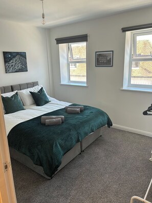 Quarto com cama, duas janelas, um quadro na parede e luminária.