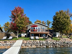 Ein Objekt am Wasser mit einer Terrasse, Liegestühlen und einem Haus mit einem roten Sonnenschirm.