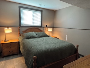A bedroom with a bed, two bedside lamps, a nightstand, a window, and a wall-mounted shelf.