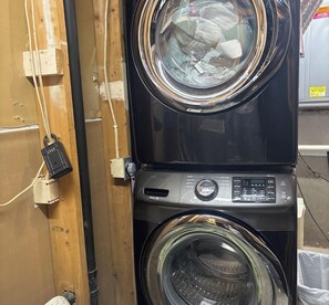 A front-loading washing machine with a control panel, a dryer, and a power cord plugged into a wall socket.