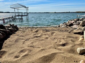 Ein sandiger Strand mit einem Steg, der sich ins Wasser erstreckt, umgeben von Felsen.