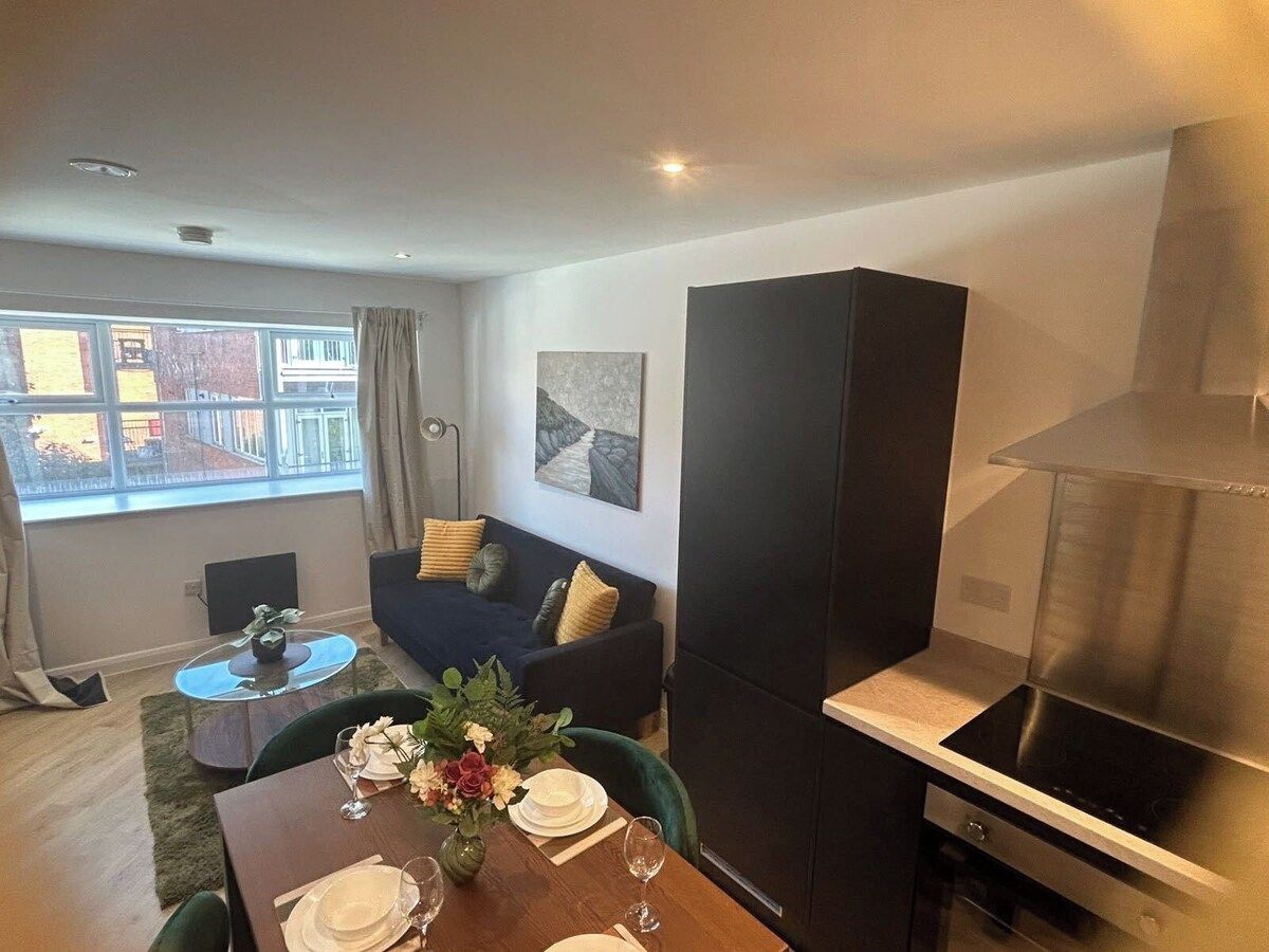 A modern living room with a dining area, a sofa, a painting on the wall, and a kitchen with a stove.