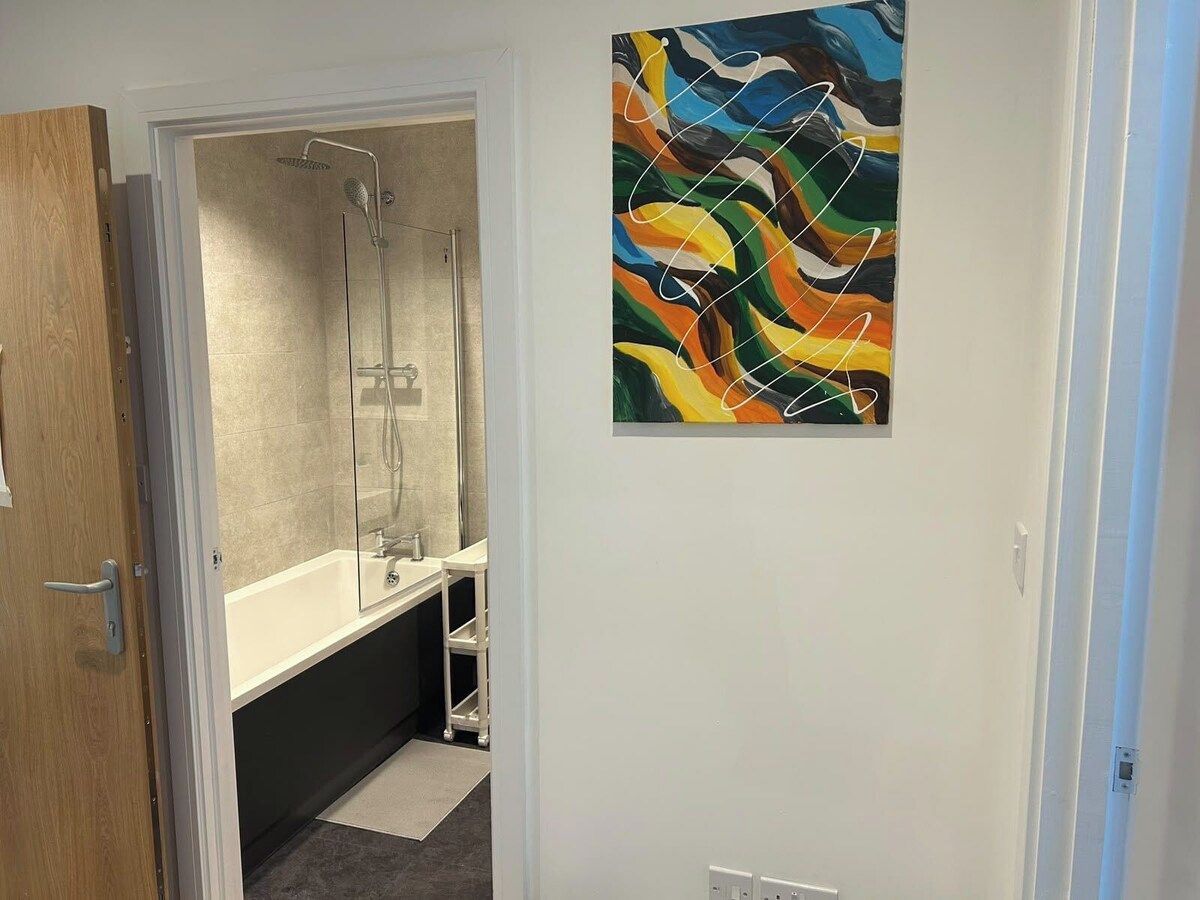 Casa de banho com chuveiro, banheira e sanita. Há um quadro na parede.