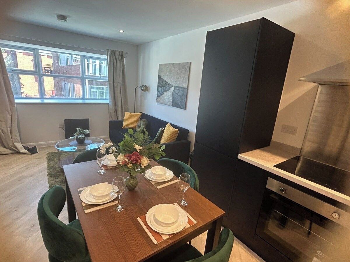 A dining area with a table set for four, a modern kitchen with a stainless steel range hood, and a view of the outside through a window.