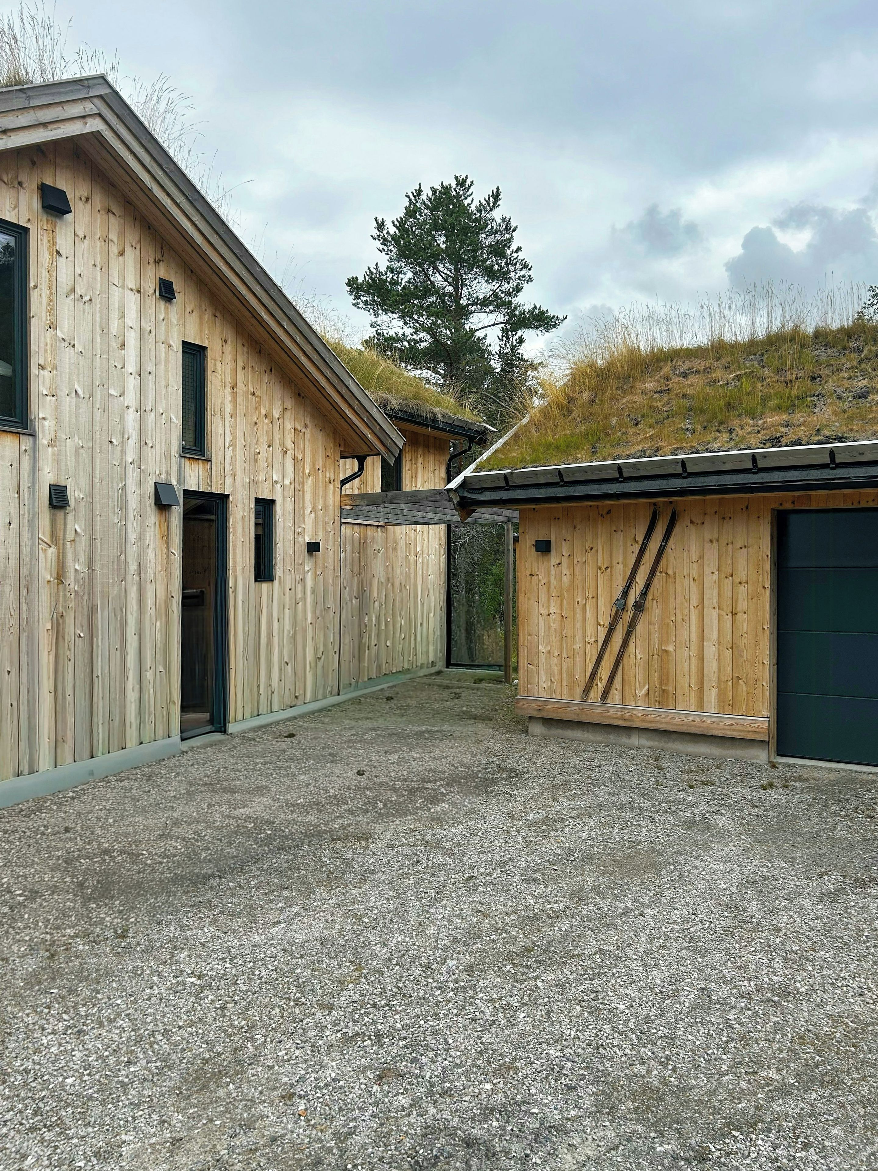 Een houten gebouw met een grindpad en een heuvel begroeid met gras op de achtergrond.