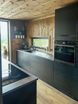 Een moderne keuken met een houten plafond, inbouwapparatuur en een raam met uitzicht op groen.