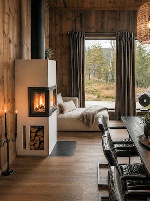 Een gezellige kamer met een open haard, een bank, een eettafel en uitzicht op het omliggende landschap.