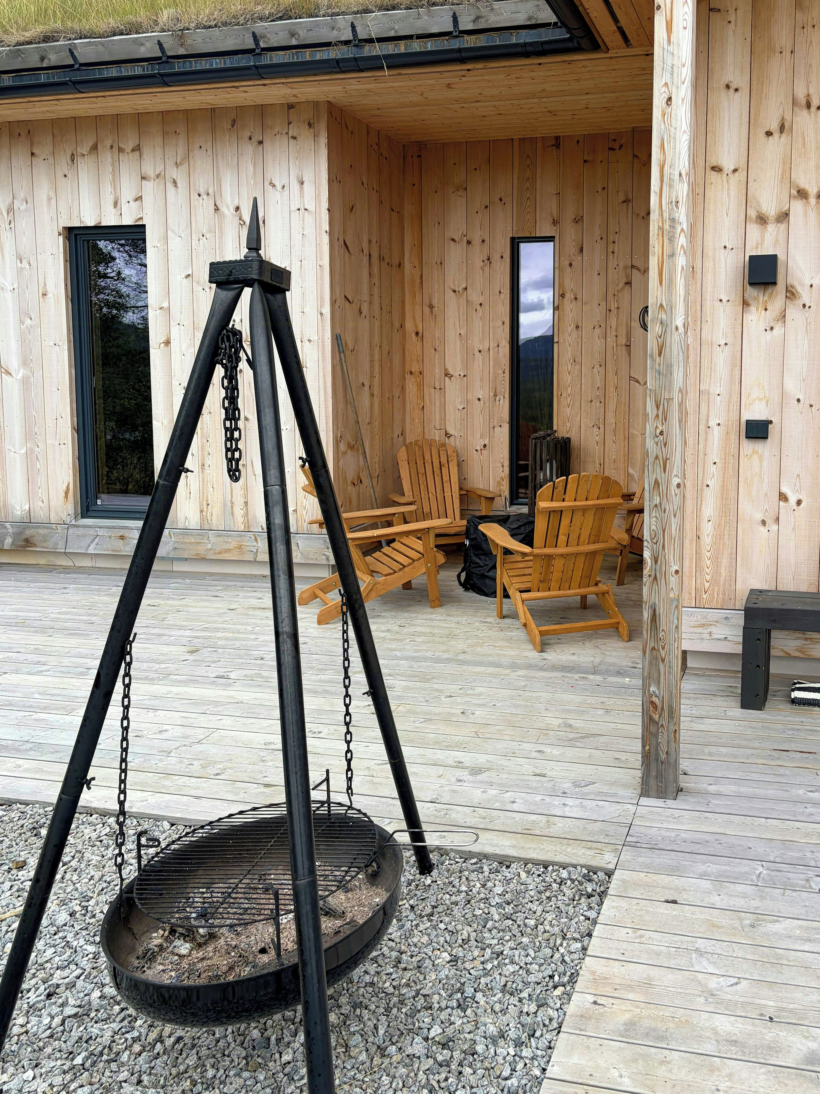 Una terrazza esterna in legno con un'altalena, due sedie di legno e una panchina.