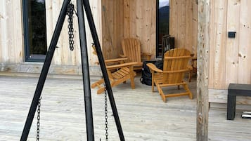 Una terrazza esterna in legno con un'altalena, due sedie di legno e una panchina.