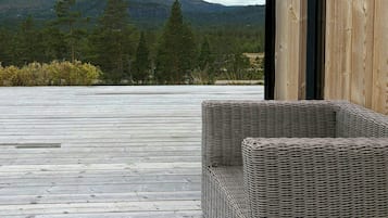 Une terrasse en bois avec un fauteuil en osier, offrant une vue sur un paysage montagneux.