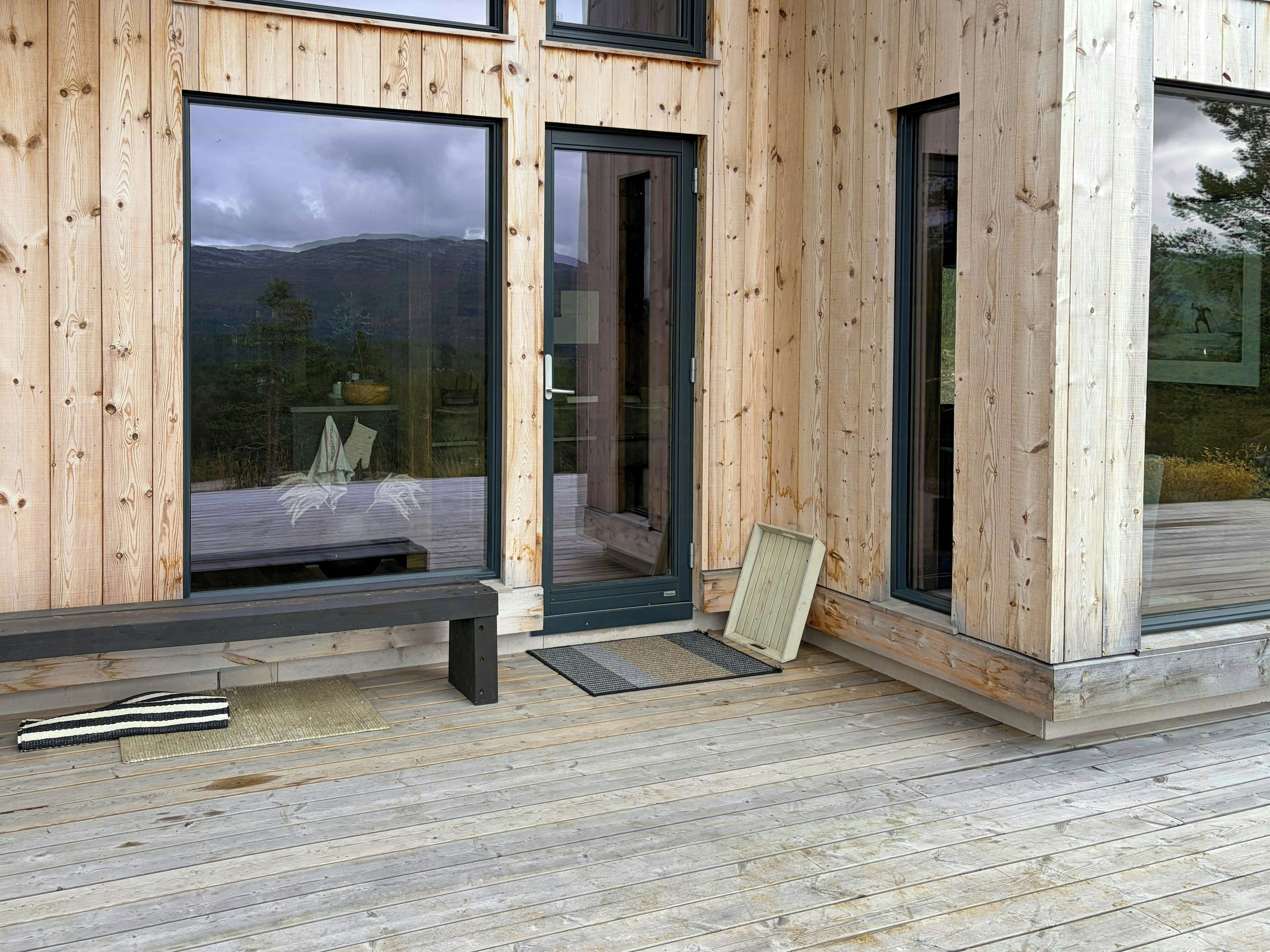 Une structure extérieure en bois, dotée de grandes fenêtres, d’un banc et d’une porte.