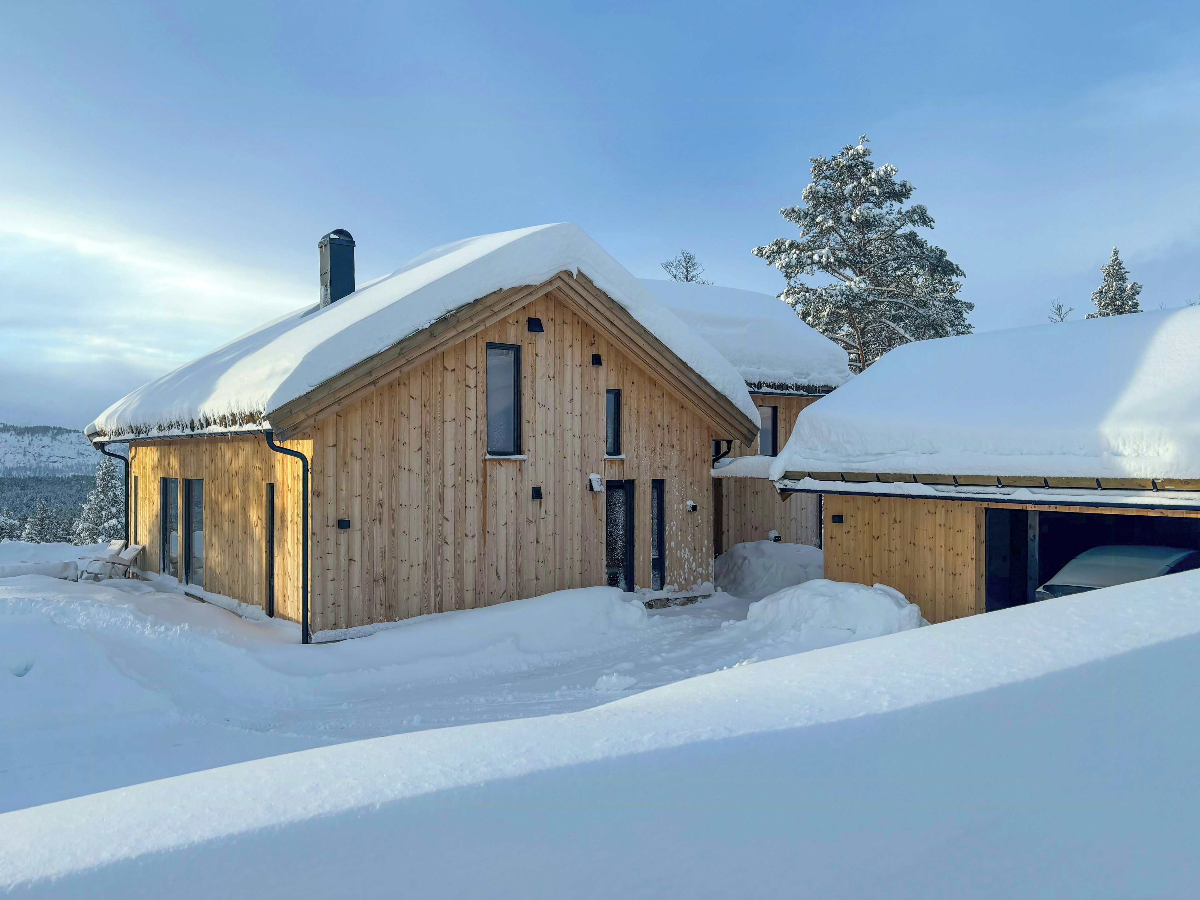 Eine Holzhütte mit schneebedecktem Dach, Schornstein und Garage.