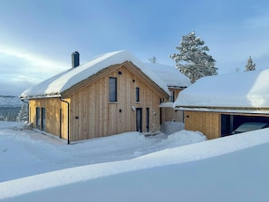Een houten blokhut met een sneeuwbedekte kap, schoorsteen en garage.