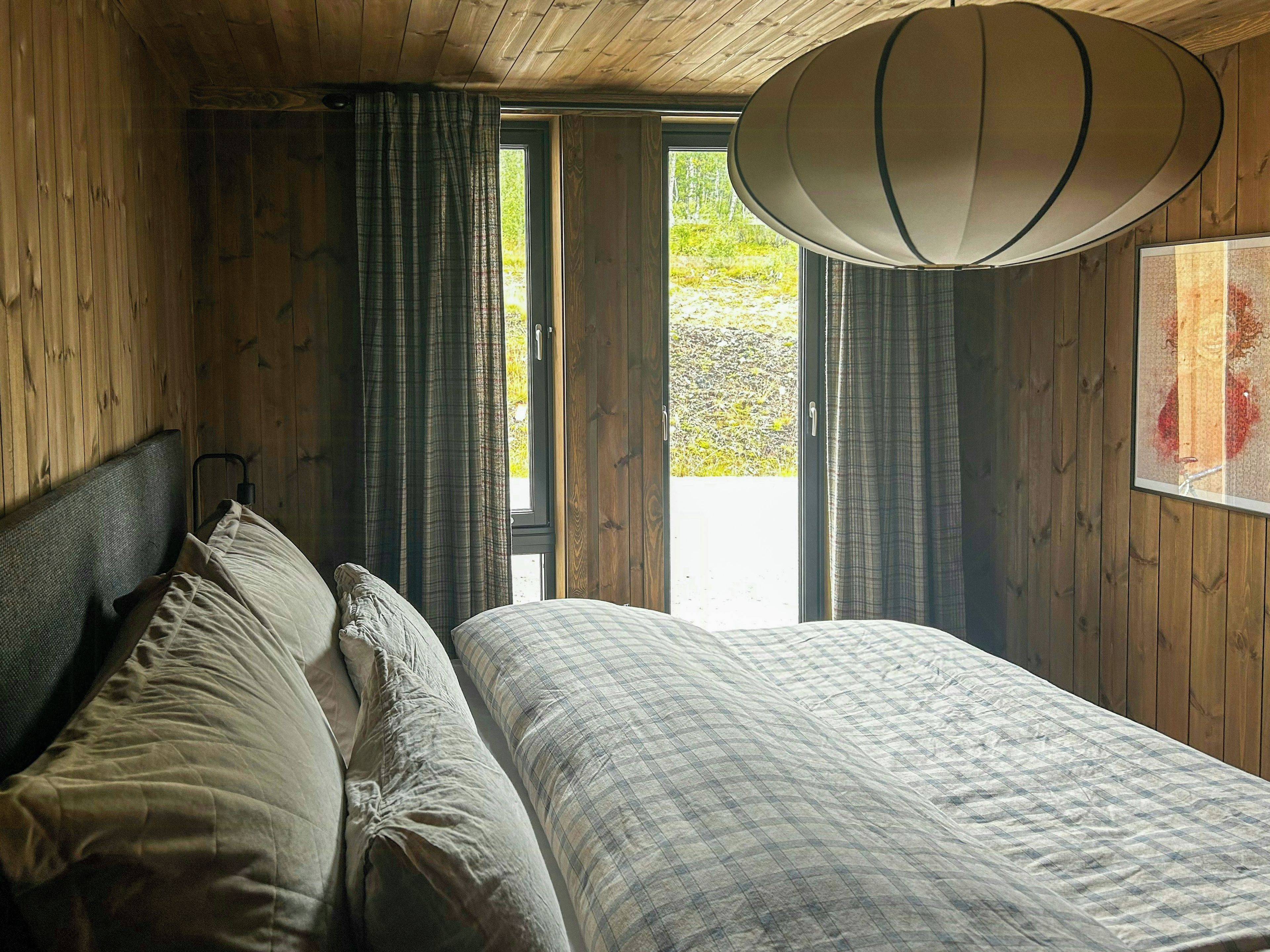 Una stanza con un letto, tende, una finestra e una lampada a sospensione.