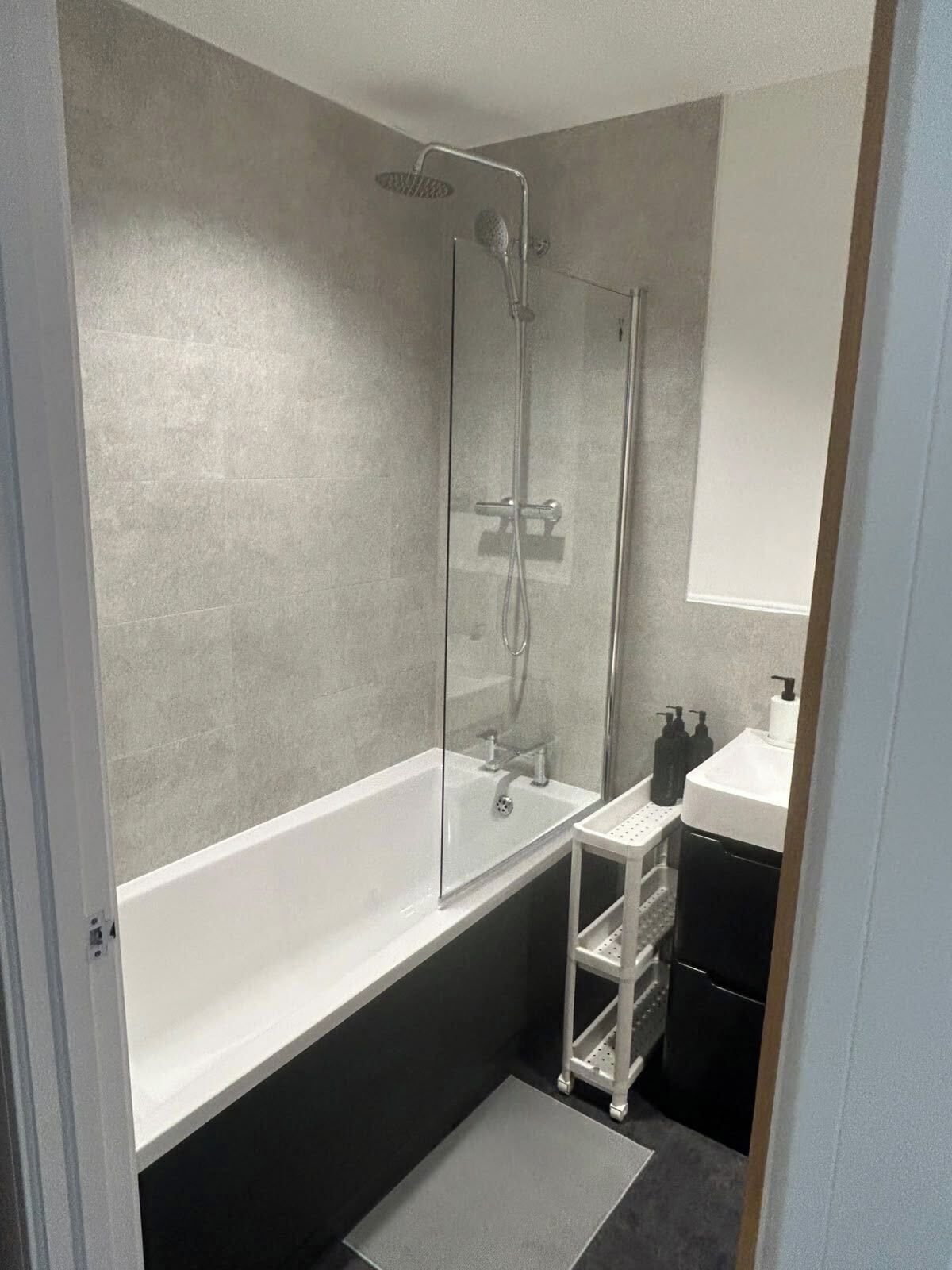 A bathroom with a glass-enclosed shower, a white bathtub, a sink with a mirror, and a small shelf with toiletries.