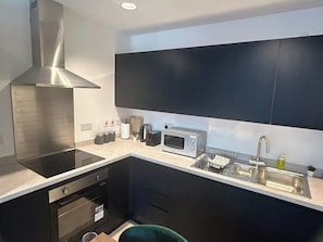 A compact kitchen with a stainless steel range hood, a microwave, and a sink. - 1BR Flat in Andover | Near Amenities & Transports (Hampshire)